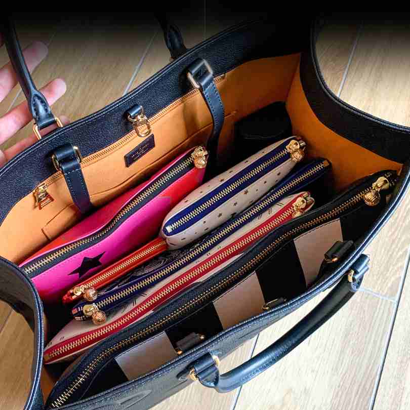 A big black leather tote bag with 6 bags organized on the inside with varying colors and styles. All have gold zipper and zipper pull 