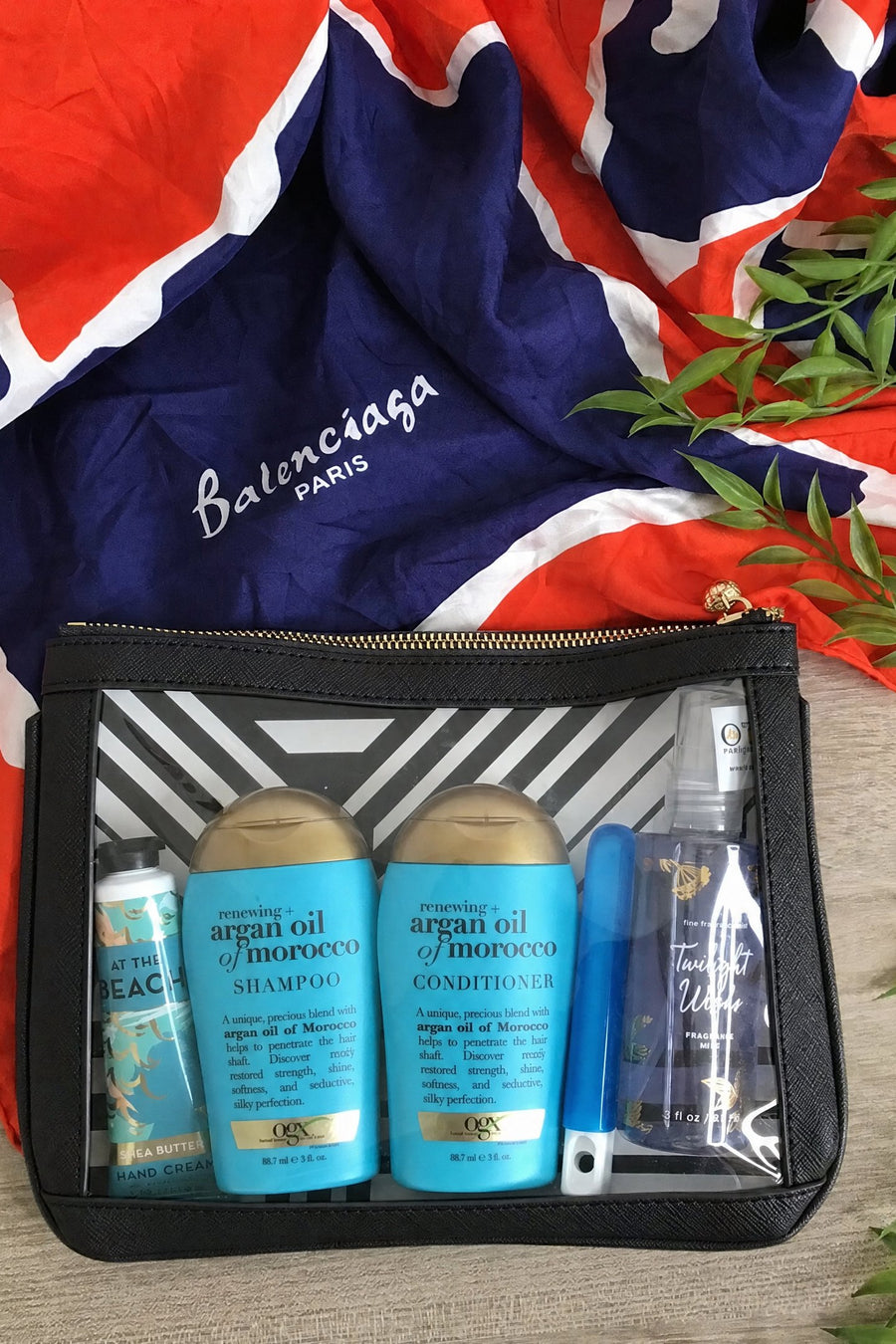 Black #4 Nudie clear-window pouch packed with travel-size shampoo, conditioner and sunscreen, styled on a silk scarf
