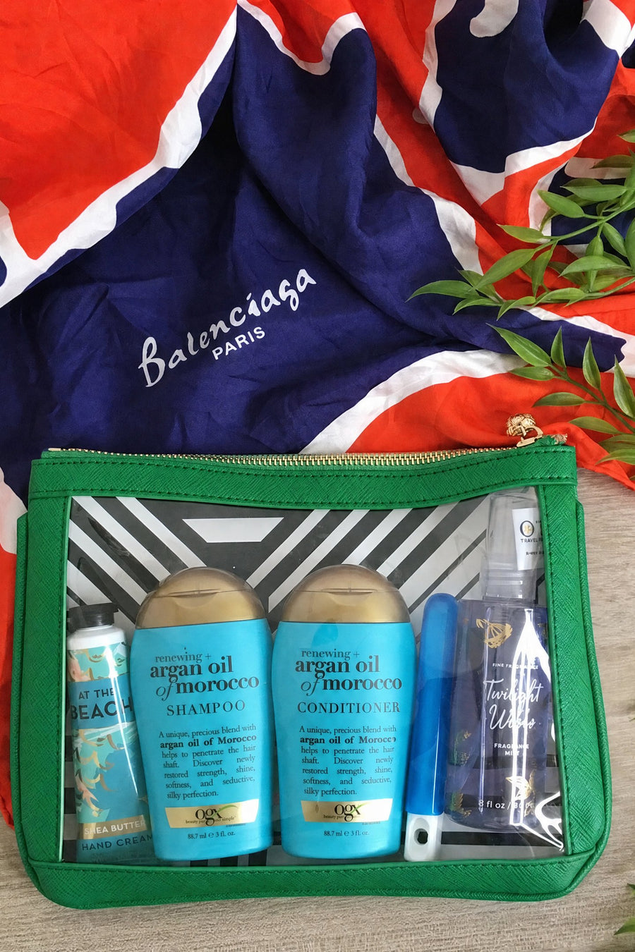 Green #4 Nudie clear-window pouch packed with travel-size shampoo, conditioner and sunscreen, styled on a silk scarf