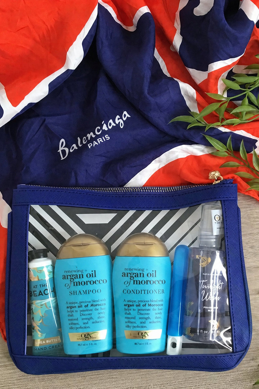Navy #4 Nudie clear-window pouch packed with travel-size shampoo, conditioner and sunscreen, styled on a silk scarf